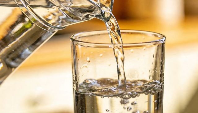 Pouring water into glass with sparkling bubbles warm golden kitchen bokeh