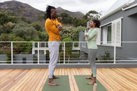 Black couple doing rooftop yoga stretches on mats with mountain backdrop