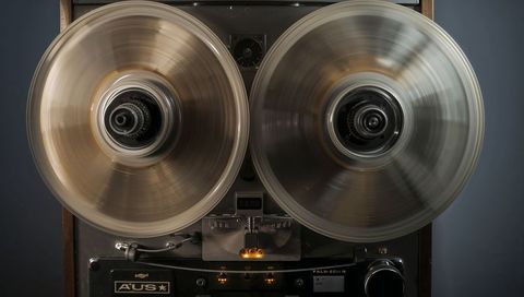 Spinning vintage reel-to-reel deck with clear acrylic reels, amber indicator lights