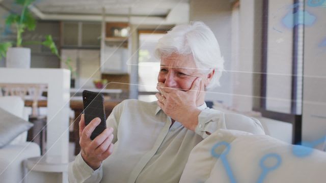 Senior woman appearing surprised and emotional while using smartphone at home. Suitable for topics related to technology for seniors, communication, digital connectivity, user engagement, and emergent life events. Can be used to illustrate emotion and connection dynamics in marketing or storytelling content.