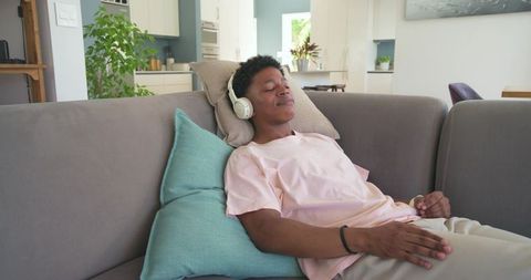African american young man listening to music relaxing on sofa in bright modern home