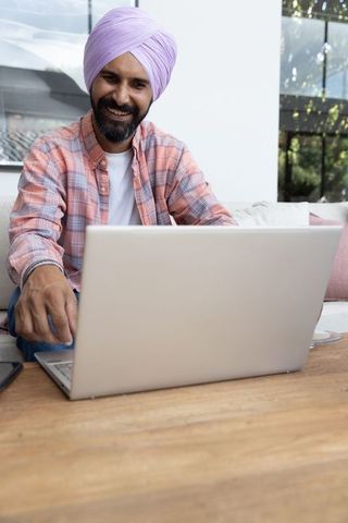 Indian man in turban smiling while using laptop at home