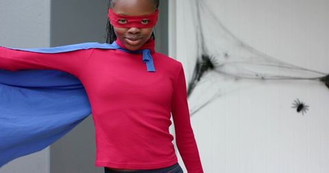 African american child wearing red mask and blue cape pretending superhero on porch