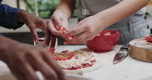 Diverse group of hands assembling homemade pizza with fresh ingredients including chopped tomatoes and cheese. Captures collaborative culinary activities in home kitchen. Ideal for use in content related to cooking, recipes, food blogs, family time, and kitchen teamwork.
