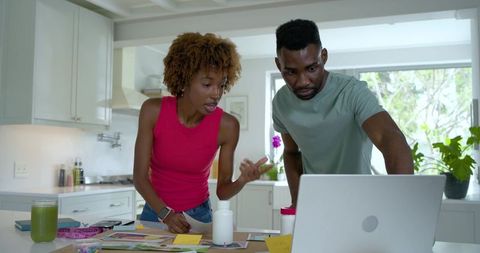 Black couple planning home business sorting prints and notes over laptop in bright kitchen