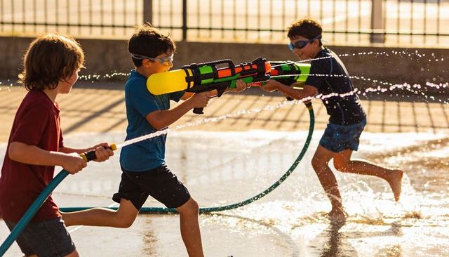 Kids running and splashing with giant water blaster on sunny pavement summer fun with hose