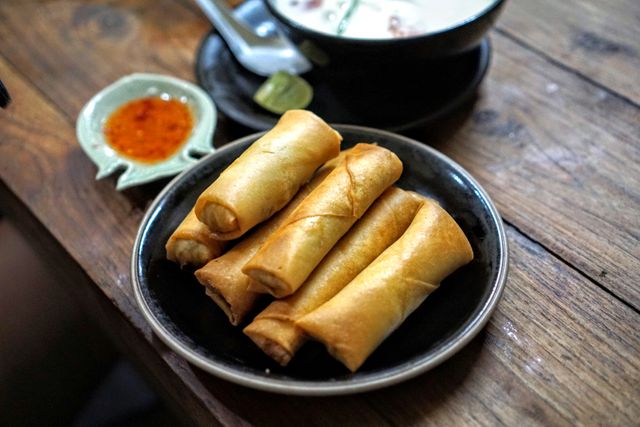 This image features a plate of crispy spring rolls served with a side of dipping sauce on a wooden table. Perfect for illustrating Asian cuisine, restaurant menus, food blogs, and culinary articles.