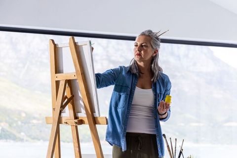Middle-aged woman painting on easel in sunlit studio with panoramic mountain view