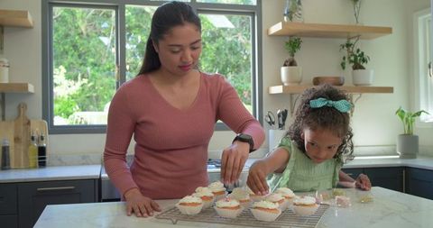 Mother and daughter decorating cupcakes together in bright home kitchen