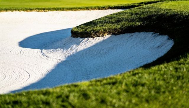 Curved raked sand bunker revealing sculpted grass lip and shadow on manicured golf green