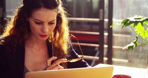 Focused young woman working on laptop in bright cafe