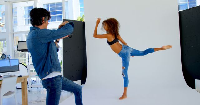 Photographer capturing a dancer performing a dynamic pose in jeans at a modern studio. This image highlights the subjects' creativity and professional environment. It is ideal for use in articles or advertisements about fashion photography, professional studios, or creative workspaces.