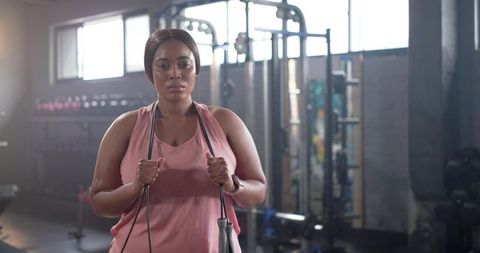 Focused african american woman training with resistance band in industrial gym, backlit