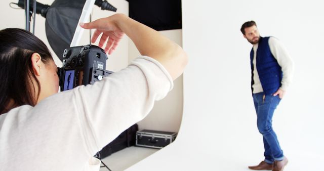 A female photographer is directing a Caucasian male model during a photoshoot, with copy space. He appears to be a young adult, dressed casually, and is posing while the photographer captures the images.