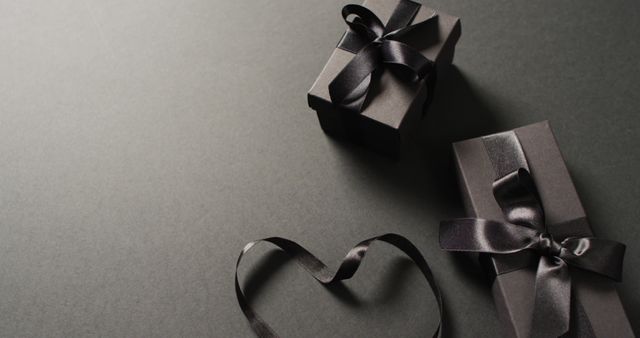 Two black gift boxes with black ribbons and ribbon in heart shape, on dark grey with copy space. Luxury treat, present, shopping, black friday sale and retail concept digitally generated image.