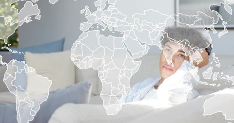 Young man relaxing on white sofa with translucent world map overlay and soft pastel light