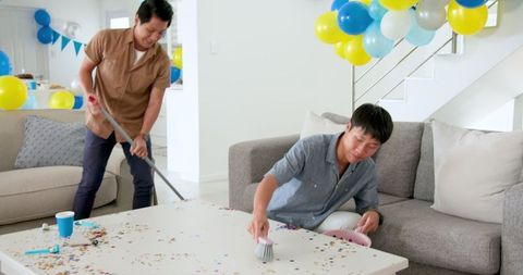 Two asian men cleaning confetti after celebration in living room