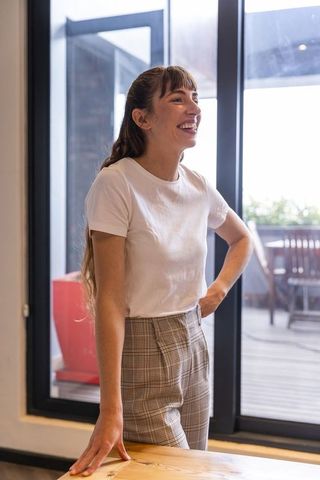 Cheerful woman in casual attire relaxing at home by large glass door