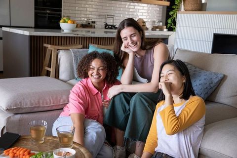 Diverse female friends laughing on cozy living room sofa