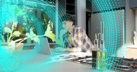 Young man working on laptop at kitchen island wearing earbuds and plaid shirt