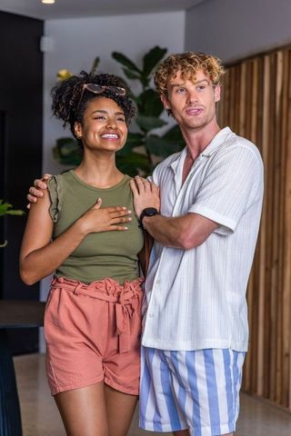 Smiling diverse couple embracing in modern home with greenery and casual summer outfits