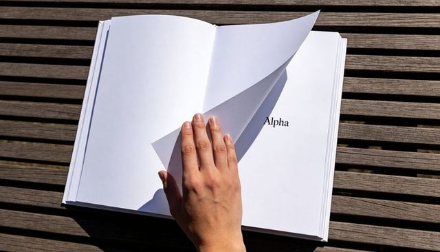 Hand turning thick book page on wooden slatted table revealing printed word alpha