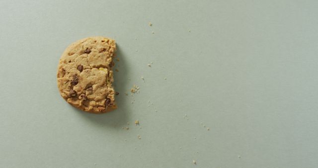 Half-eaten chocolate chip cookie placed on light grey background with crumbs scattered nearby. Useful for depicting snacking, sweet treats, or dessert concepts. Ideal for food blogs, advertisements, and recipes.