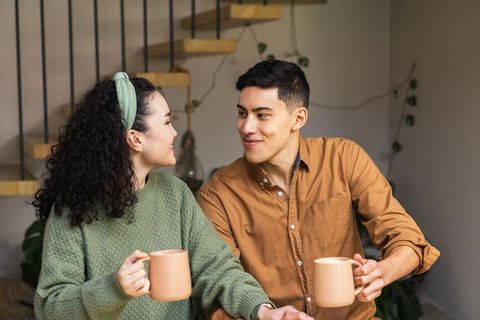Young couple sharing coffee and smiling in cozy modern home with wooden floating staircase