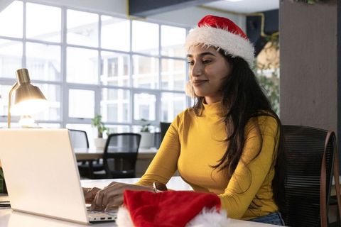 Indian woman wearing santa hat working on laptop in modern coworking space