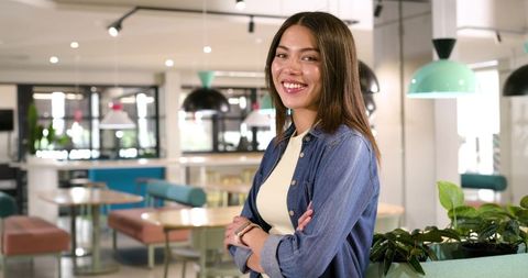 Confident african american woman standing with arms crossed in modern coworking cafe