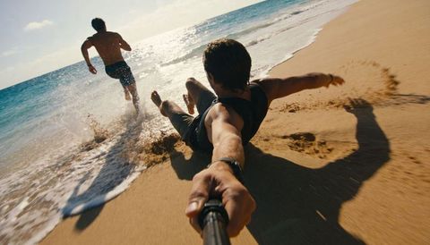 Sliding on shoreline with selfie stick while friend runs into ocean - beach adventure