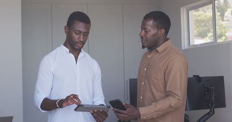 Men collaborating using tablet and smartphone in modern office