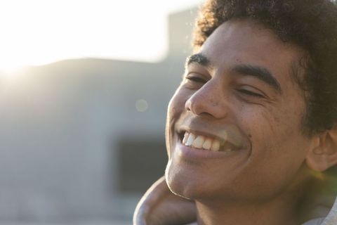 African american man smiling in golden hour backlit rooftop portrait with hoodie and lens flare