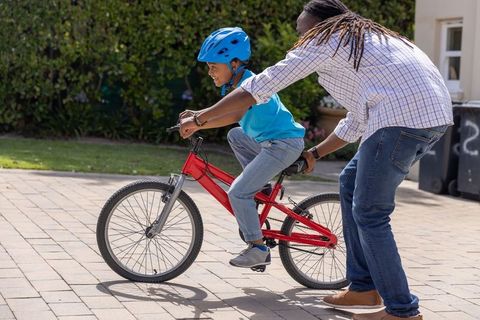 African american father teaching son to ride red bicycle on sunlit suburban driveway