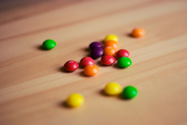 Colorful candy pieces scattered across a wooden table, showing vibrant bright colors and a playful arrangement. Ideal for illustrations, digital marketing materials, or food and snack-related content.