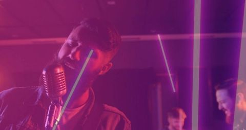 Bearded vocalist singing into vintage microphone on magenta lit stage with LED light tubes