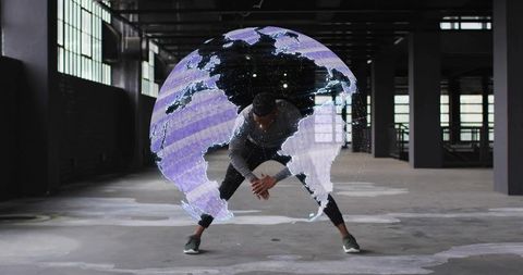 Crouching athlete activating holographic globe projection in industrial warehouse futuristic tech