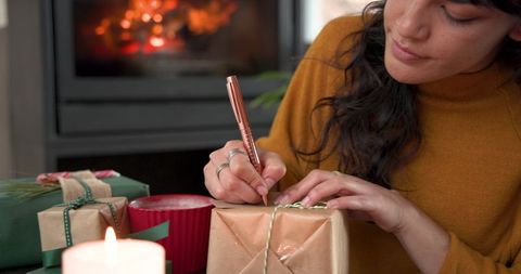 Woman writing gift tag by cozy fireplace during holiday season