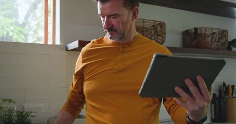 Mature man cooking in kitchen while using tablet for recipe