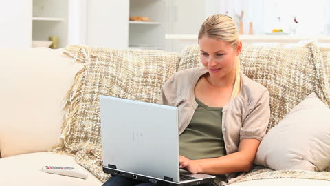 Smiling Woman Lounging on Sofa While Using Laptop