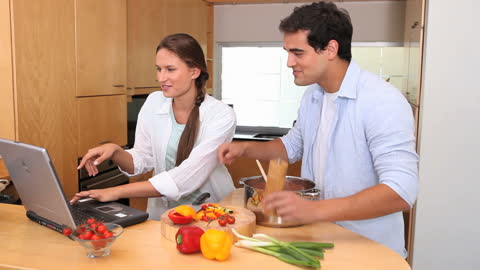 Smiling Couple Cooking and Using Laptop in Modern Kitchen