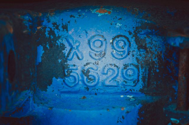 Engraved blue industrial metal showing X99 and 5629 in close-up view. Ideal for illustrating industrial processes, machinery parts, or manufacturing themes. Perfect for design projects that focus on grunge aesthetics, texture studies, or factory environments.