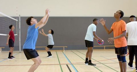 Diverse men practicing indoor volleyball passing and teamwork during gym training