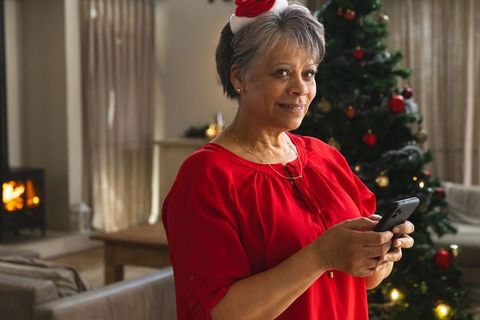 Smiling Elderly Woman Using Smartphone by Christmas Tree