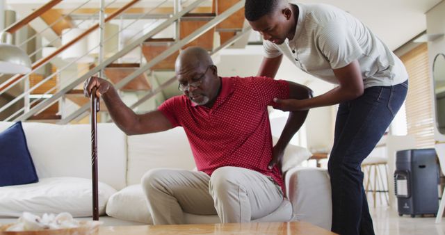 African american senior father getting up the couch and using a cane with teenage son helping - Download Free Stock Photos Pikwizard.com