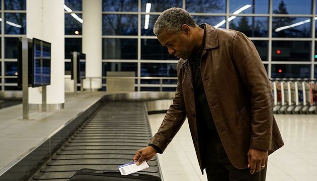 Traveler picking up suitcase at airport baggage claim holding boarding pass during dusk