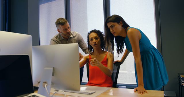 Three coworkers are gathered around a desk, engaged in an intense discussion while looking at a computer screen. Ideal for depicting teamwork, office collaboration, business discussions, project planning, and professional environments.
