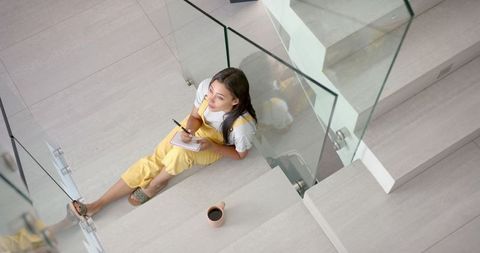Girl in yellow overalls writing on stairs with coffee break