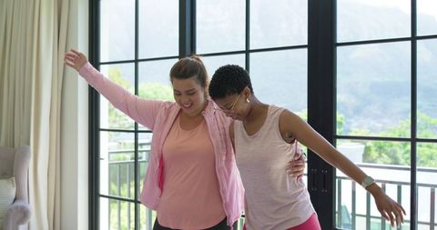 African american women balancing and laughing near sunlit grid windows in casual athleisure