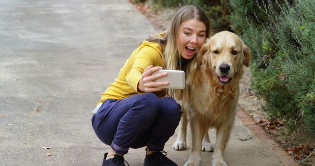 Young woman taking a selfie with her golden retriever on a path surrounded by greenery. Suitable for topics related to pets, bonding, outdoor activities, happiness, and casual lifestyle.